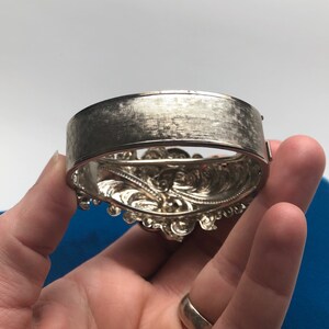 K&ouml;nnte beinhalten: Silberarmband mit einem verzierten, detaillierten Design. Das Armband ist offen und hat eine glatte, geb&uuml;rstete Oberfl&auml;che auf der R&uuml;ckseite.