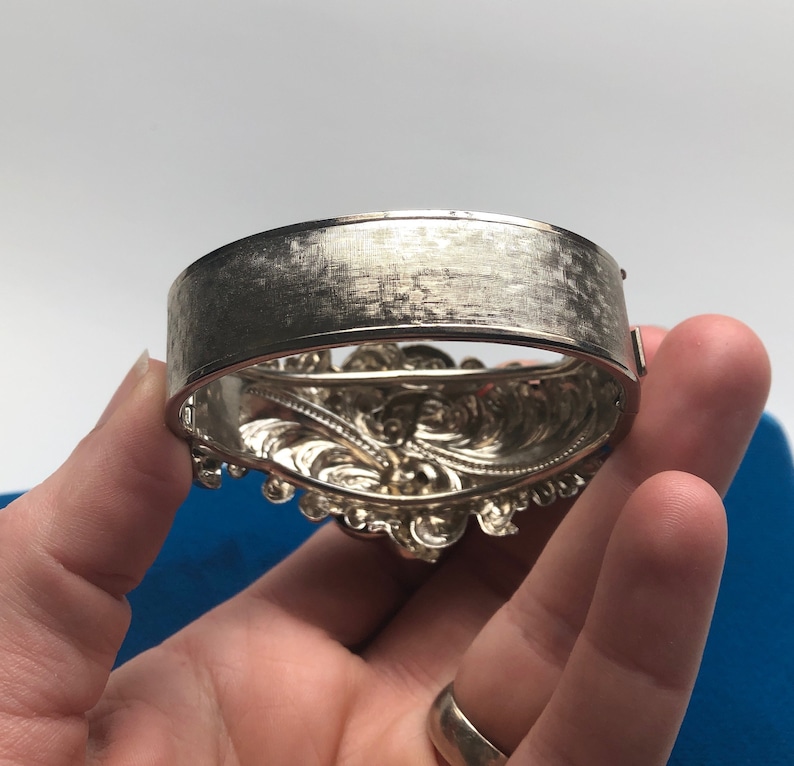 K&ouml;nnte beinhalten: Silberarmband mit einem verzierten, detaillierten Design. Das Armband ist offen und hat eine glatte, geb&uuml;rstete Oberfl&auml;che auf der R&uuml;ckseite.