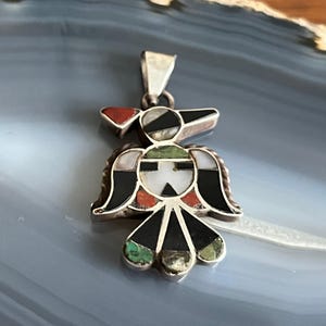 Peut inclure: Un pendentif en argent représentant un oiseau stylisé avec des incrustations complexes de turquoise, rouge, noir et blanc.