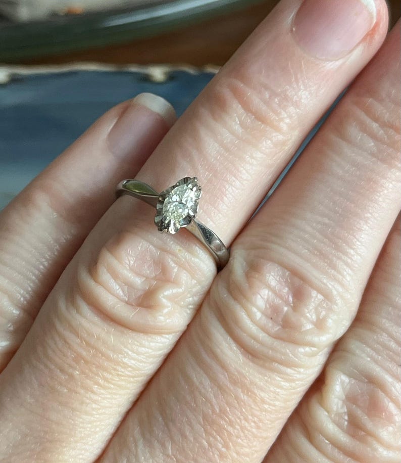 Puede incluir: Un anillo de plata con un diamante de forma marquesa engastado en garras.