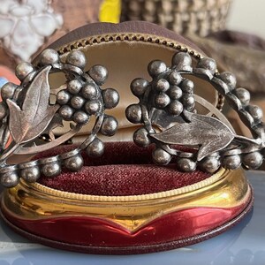 May include: A pair of silver tone earrings with a grapevine design. The earrings are in a velvet lined box.
