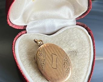 May include: A gold-colored oval locket with a vertical striped pattern and the letter "I" is displayed inside a heart-shaped red box. The box is lined with white satin and has the text "H. Hoy, Branthwaite Brow, KENDAL" printed on the inside.