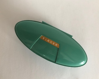 May include: A green plastic sewing machine needle case with the word "SINGER" printed in gold letters.