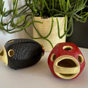 May include: Two ceramic fish-shaped planters, one black with a textured surface and one red with a yellow mouth and eyes.