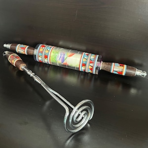 May include: A colorful rolling pin with a wooden handle and a clear acrylic barrel with a floral design. A silver metal potato masher with a spiral head and a wooden handle.