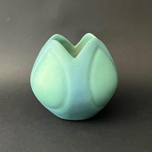 Op de afbeelding: Een kleine, afgeronde vaas in tinten blauw en groen. De keramische vaas heeft een unieke, bloembladachtige vorm met een brede opening. Het gladde oppervlak heeft een gradiënteffect, dat overgaat van lichtgroen naar dieper blauw.