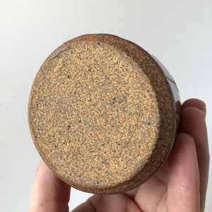 Puede incluir: Una taza de cer&aacute;mica marr&oacute;n con un esmalte moteado. La taza tiene un fondo redondeado y un labio ligeramente acampanado.