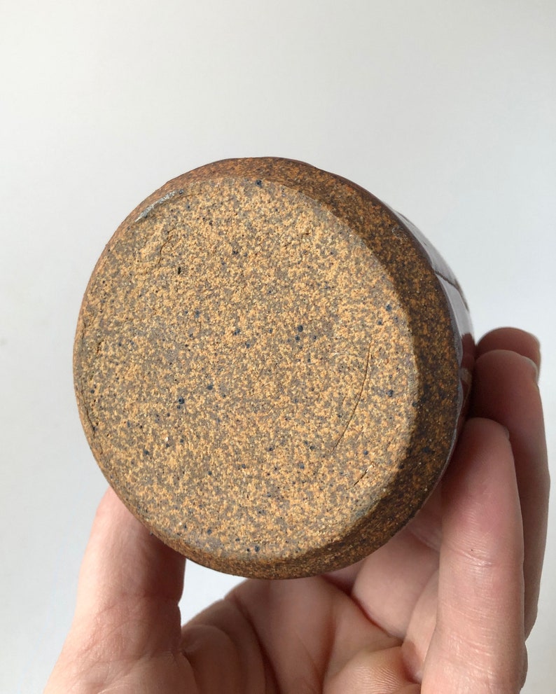 Puede incluir: Una taza de cer&aacute;mica marr&oacute;n con un esmalte moteado. La taza tiene un fondo redondeado y un labio ligeramente acampanado.