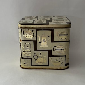 Puede incluir: Lata de té cuadrada de metal vintage con un patrón repetido de teteras negras y doradas sobre un fondo crema. La tapa también está decorada con siluetas de teteras. La lata tiene un aspecto ligeramente envejecido.