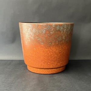 May include: A ceramic plant pot with a textured, speckled finish. The pot has a colour gradient, shifting from a dark, earthy tone at the top to a bright orange at the base. It has a wide, cylindrical shape with a slightly flared rim and a raised base.