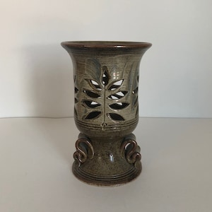 May include: A ceramic vase with a leafy design and a brown glaze. The vase has a wide base with three decorative feet.