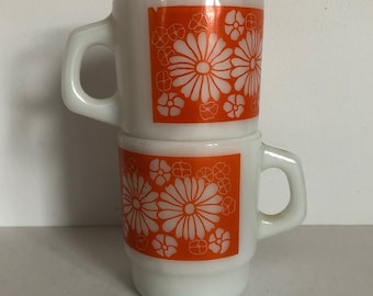 Paar Fire King melkglas stapelkoffiemokken oranje madeliefje