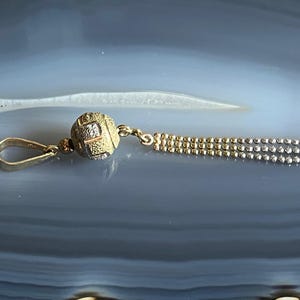 Puede incluir: Un colgante de oro con un dije de bola texturizada y una cadena con cuentas alternas de oro y plata.
