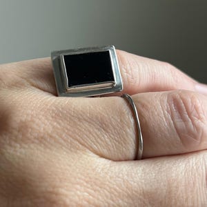 May include: A silver ring with a black rectangular stone set in a silver frame.