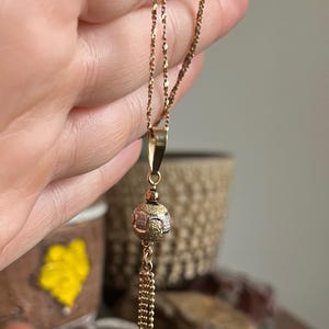Puede incluir: Un collar de cadena de oro con un colgante redondo con un dise&ntilde;o texturizado. El colgante est&aacute; unido a una cadena de borla.