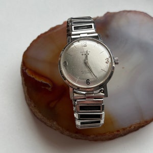 May include: A silver Benrus self-winding watch with a white face and black hands. The watch has a silver metal band with black accents.