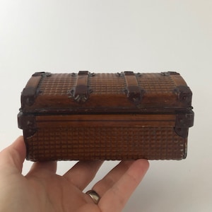 May include: A small, brown, metal treasure chest with a woven pattern and metal accents. The chest is closed and has a hinged lid.