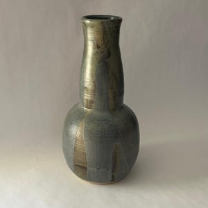 May include: A handcrafted ceramic vase with a bulbous base and a slender neck. The vase features a metallic gold and gray glaze, with vertical streaks of gold against a gray background. The vase is approximately 8 inches tall.