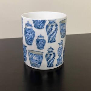 Puede incluir: Taza de cer&aacute;mica blanca con un patr&oacute;n repetido de jarrones antiguos azules y blancos. La taza tiene forma cil&iacute;ndrica y un acabado liso y brillante. El dise&ntilde;o incluye varias formas y tama&ntilde;os de jarrones.