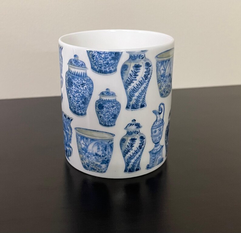 Puede incluir: Taza de cer&aacute;mica blanca con un patr&oacute;n repetido de jarrones antiguos azules y blancos. La taza tiene forma cil&iacute;ndrica y un acabado liso y brillante. El dise&ntilde;o incluye varias formas y tama&ntilde;os de jarrones.