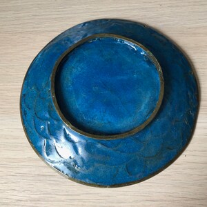 May include: A blue ceramic plate with a brass rim and a decorative design. The plate has a raised rim and a smooth surface.