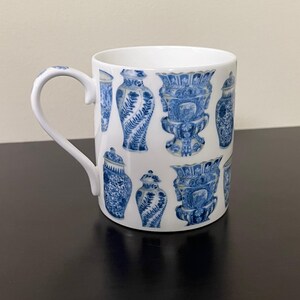 Puede incluir: Taza de cer&aacute;mica blanca con un patr&oacute;n repetido de jarrones decorativos azules y blancos. La taza tiene un asa curva y un acabado brillante. El dise&ntilde;o incluye varias formas de jarrones con intrincados patrones florales y geom&eacute;tricos.