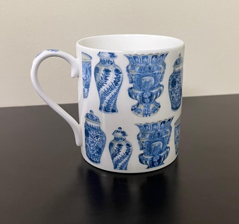 Puede incluir: Taza de cer&aacute;mica blanca con un patr&oacute;n repetido de jarrones decorativos azules y blancos. La taza tiene un asa curva y un acabado brillante. El dise&ntilde;o incluye varias formas de jarrones con intrincados patrones florales y geom&eacute;tricos.