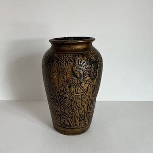 May include: A brown ceramic vase with an embossed design of people and trees. The vase has a slightly flared top and a rounded bottom.
