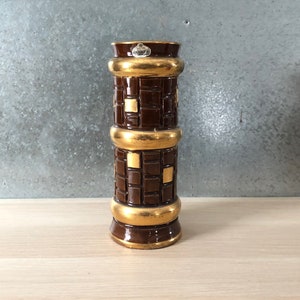 Peut inclure: Un vase en céramique brun avec des accents dorés et un motif géométrique. Le vase a une forme cylindrique et est décoré d'un motif répétitif de carrés.