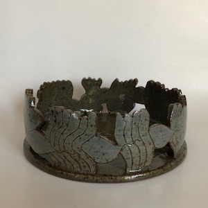 Puede incluir: Un cuenco de cerámica con un diseño decorativo de hojas estilizadas alrededor del borde. El cuenco es de color gris claro con acentos marrones.