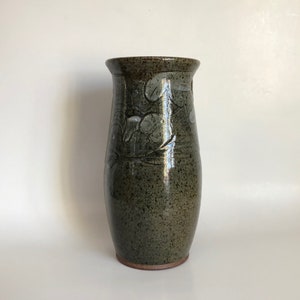 May include: A green ceramic vase with a speckled glaze and a white floral design.