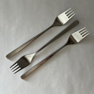 May include: Three stainless steel forks with a simple, modern design. Each fork has four tines and a long, slender handle. The forks are arranged diagonally against a white background, showcasing their polished, reflective surfaces.