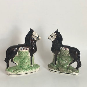 May include: Two brown ceramic horse figurines with white markings. Each horse is standing on a green base with a basket of flowers. The horses are facing each other.