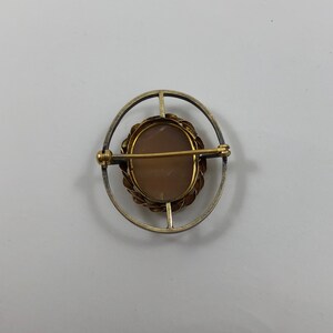 May include: A silver and gold oval brooch with a cameo set in a gold frame. The cameo is a light brown color and has a detailed design.