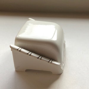 K&ouml;nnte beinhalten: Eine wei&szlig;e Keramik-Butterdose mit Deckel und einem dekorativen Design an der Seite.