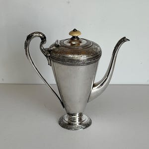 May include: A silver teapot with an ornate design and a bone-colored knob on the lid.