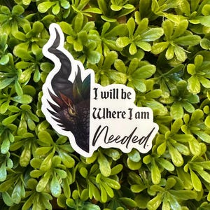 May include: A white sticker with a dragon head design and the text "I will be Where I am Needed." The dragon has a black horn and a red and brown eye. The sticker is set against a background of green leaves.