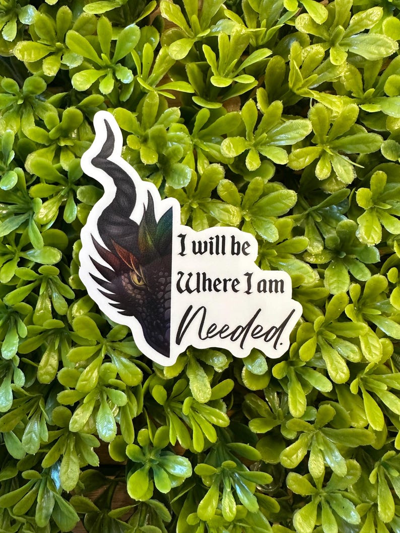 May include: A white sticker with a dragon head design and the text "I will be Where I am Needed." The dragon has a black horn and a red and brown eye. The sticker is set against a background of green leaves.