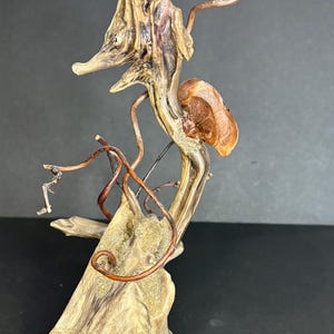 May include: A unique, abstract sculpture crafted from natural wood and copper wire. The sculpture features a seahorse-like form with intricate details, including a textured wooden base and delicate copper tendrils. The color palette includes shades of brown, beige, and copper.