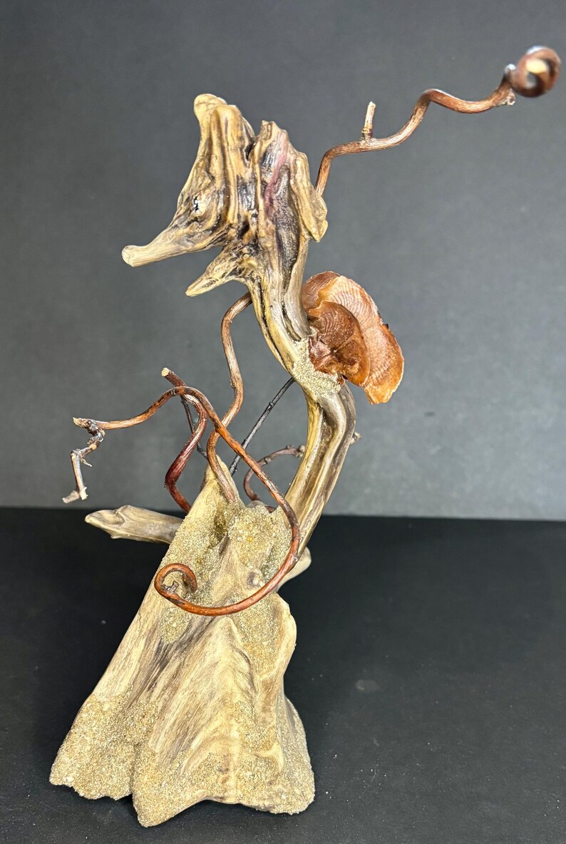 May include: A unique, abstract sculpture crafted from natural wood and copper wire. The sculpture features a seahorse-like form with intricate details, including a textured wooden base and delicate copper tendrils. The color palette includes shades of brown, beige, and copper.