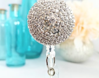 May include: A silver retractable badge holder with a large round rhinestone embellishment. The rhinestones are clear and sparkle.