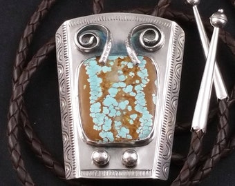 May include: A silver bolo tie with a turquoise stone set in a silver frame. The bolo tie has a brown leather cord.