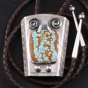 May include: A silver bolo tie with a turquoise stone set in a silver frame. The bolo tie has a brown leather cord.