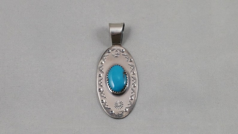 Pode incluir: Um pingente de prata com uma pedra turquesa engastada em forma oval. O pingente &eacute; decorado com uma borda de prata e desenhos intrincados.