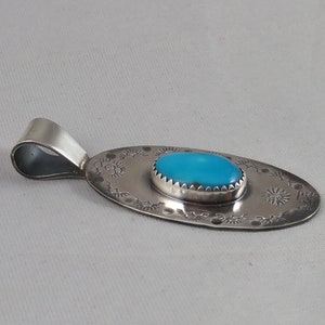 Pode incluir: Um pingente de prata com uma pedra turquesa ovalada engastada em uma moldura de prata. O pingente &eacute; decorado com um design de prata em torno da pedra e na parte de tr&aacute;s.