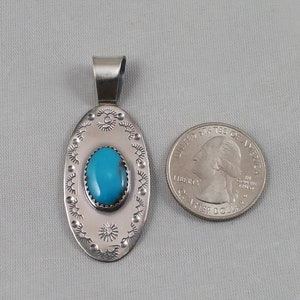Pode incluir: Pingente de prata com uma pedra turquesa engastada em forma oval. O pingente &eacute; rodeado por uma borda decorativa. O pingente &eacute; aproximadamente do tamanho de uma moeda de 25 centavos.