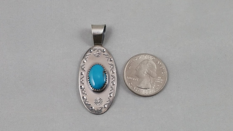 Pode incluir: Pingente de prata com uma pedra turquesa engastada em forma oval. O pingente &eacute; rodeado por uma borda decorativa. O pingente &eacute; aproximadamente do tamanho de uma moeda de 25 centavos.