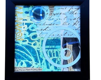 Puede incluir: Obra de arte abstracta enmarcada en negro. La obra presenta un collage de elementos azules, turquesas y dorados con texto manuscrito y recortes circulares. La palabra "MEMORY" es visible en letras doradas.