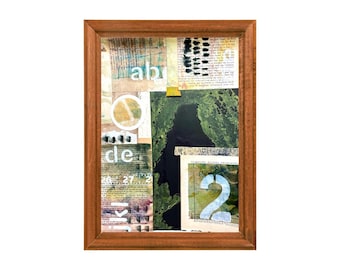 Könnte beinhalten: Eine gerahmte Mixed-Media-Collage mit einem braunen Holzrahmen. Das Kunstwerk zeigt geschichtete Papierelemente, darunter Text, abstrakte Formen und die Zahl "2". Die Farben umfassen Grün, Schwarz, Weiß und Beige.