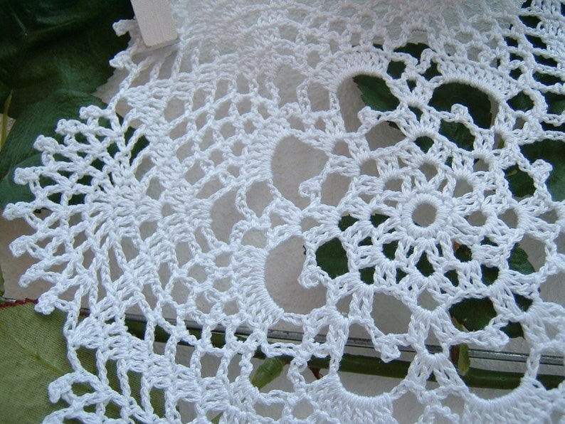 Peut inclure: Gros plan sur un napperon au crochet blanc fait &agrave; la main. Le motif de dentelle complexe pr&eacute;sente un motif floral central entour&eacute; de jours et de bords festonn&eacute;s. Le napperon est en fil blanc.
